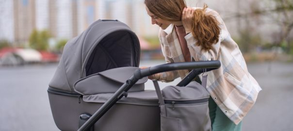 Young,Happy,Mom,Looking,Into,Stroller,With,Her,Sleeping,Baby,